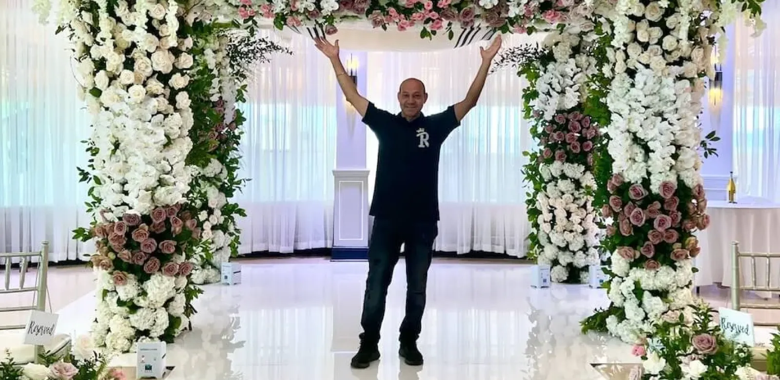 Jose Ramirez standing beneath a floral wedding arch he designed for Royal Floral Designs