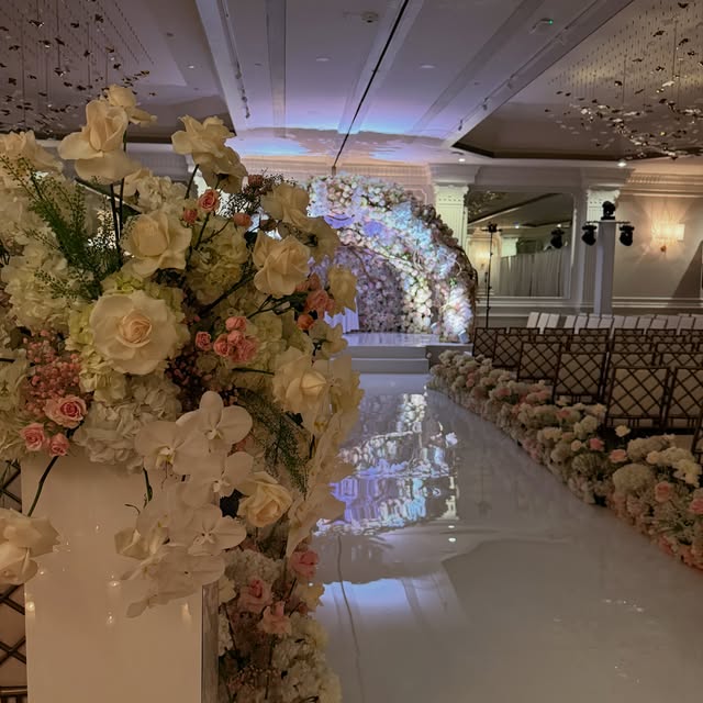 A white rose ceremony arch beside a mirrored aisle, designed by Royal Floral Designs for a ballroom wedding