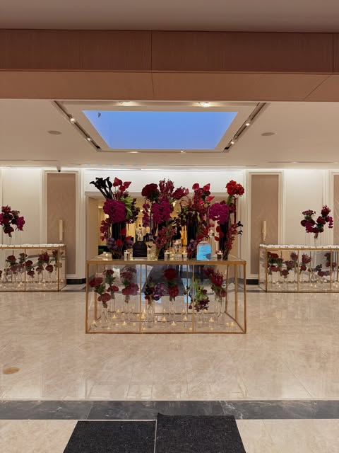 Burgundy centerpieces on glass tables in a ballroom foyer